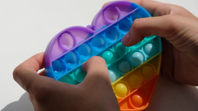 Hands play with antistress pop it toy. Rainbow sensory fidget isolated on white background. New trendy silicone toy.