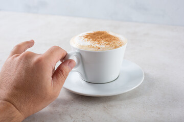 A view of a hand holding the handle of a cappuccino coffee mug.