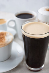 A view of a collection of popular coffee drinks in cups and glasses.