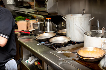 A view of a busy restaurant kitchen cooking area, featuring stockpots, grilled food and clutter.