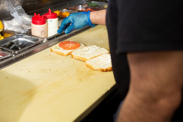 An over the shoulder view of a cook preparing a sandwich at the prep station of a restaurant kitchen.