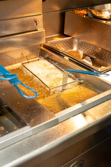 A closeup view of a food basket frying in bubbling oil, in a restaurant kitchen setting.