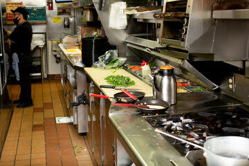 A view inside the food and order assembly area inside a restaurant kitchen. A line cook prepares food in the background.