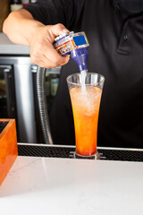 A view of a bartender behind the counter, preparing a cocktail featuring a soda fountain dispenser.