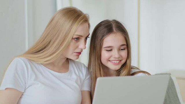 Adult beautiful mother mature woman with daughter teenage girl sitting together at home using modern laptop to watch movies funny videos on web on site browsing looking at computer screen laughing
