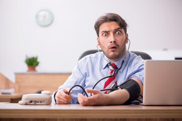 Young male employee suffering from hypertension at workplace