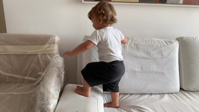 Baby toddler climbing furniture at apartment sitting down and laughing