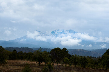 Fototapeta na wymiar mountains of puebla city, mexico freshly snowed with forest bushes in the foreground and a dramatic sky with lots of clouds.