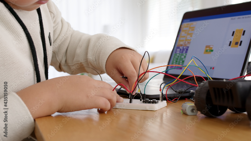 Wall mural Young asia student remotely learn online at home in coding robot car and electronic board cable in STEM, STEAM, mathematics engineering science technology computer code in robotics for kids concept.