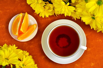 A mug of black tea, yellow chrysanthemums and orange slices.