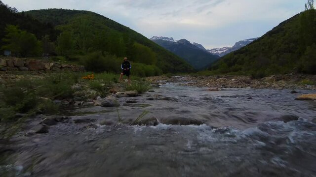 Aerial view of a fisherman in a small river in the spanish pyrenees with the snowy mountains in the background.