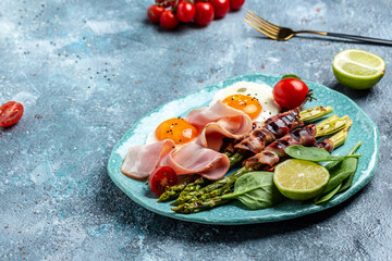 Fototapeta na wymiar Ketogenic, keto diet. brunch breakfast. fried eggs, asparagus wrapped in bacon, ham, tomatoes and salad. Healthy food