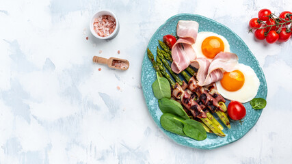 Fototapeta na wymiar Ketogenic paleo diet. Fried eggs, asparagus wrapped in bacon, ham, tomatoes and salad. Keto breakfast. Brunch. banner, menu recipe place for text, top view