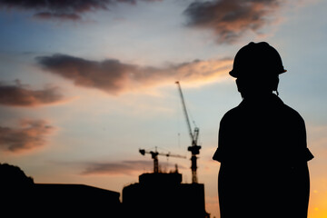 Fototapeta na wymiar The silhouette of a happy son wearing a helmet looks at the building construction at sunset 