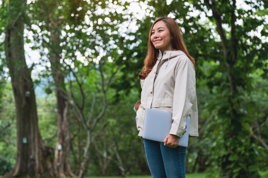 Portrait image of a beautiful young asian woman holding and using laptop computer in the outdoors