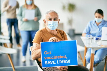 Senior man inviting people to get vaccinated against coronavirus and save lives while holding placard at vaccination center.