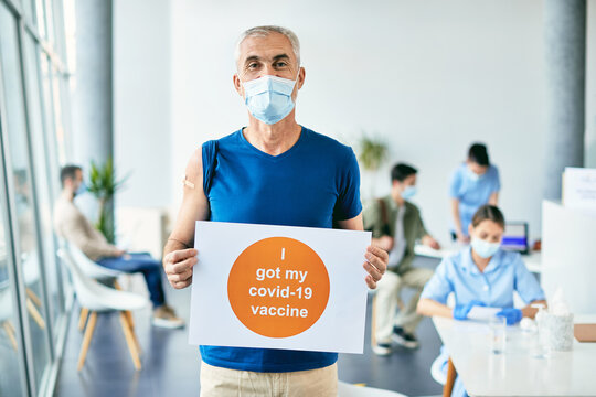 Mature man holding supportive placard during coronavirus immunization at vaccination center.