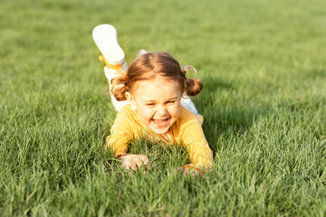 Smiling emotional child girl, lying on sunny green grass. Childhood happiness.Time to...