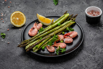 Plate with a keto diet food. baked asparagus, shrimps, green peas and lemon on black background. Keto paleo lunch, Top view