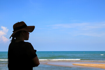 A woman in a wide-brimmed hat stands with her arms folded. Enjoy the nature of the sea and clear sky.