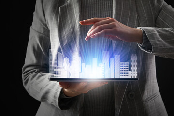Businesswoman with tablet computer and digital projection of buildings on dark background, closeup