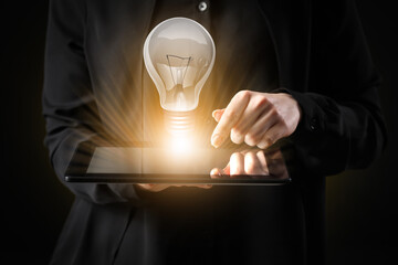 Businesswoman with tablet computer and glowing light bulb on dark background, closeup