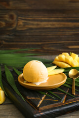Plate with tasty mango ice cream and palm leaf on wooden background