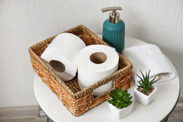 Basket with rolls of toilet paper, bottle of soap and houseplants on table in bathroom
