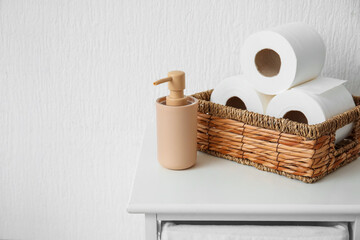 Basket with rolls of toilet paper and bottle of cosmetic product on table in bathroom