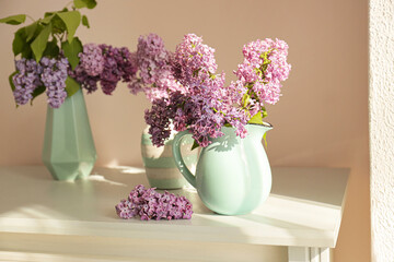 Fototapeta premium Vases with beautiful lilac flowers on table in room