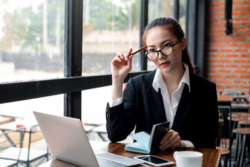 Image of a young Asian businesswoman holding a notebook and pen use think in work and a laptop at the office.