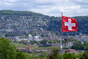 Swiss flag blowing in the wind with cityscape of Zurich in the background at springtime. Photo taken May 22nd, 2021, Zurich, Switzerland.