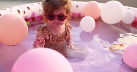 cute toddler baby girl playing with air balloons at inflatable pool at warm summer evening