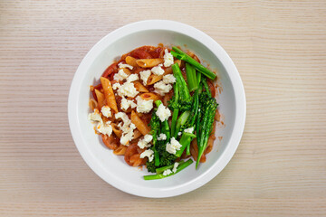 A bowl of tomato penne pasta with broccolini and feta cheese.