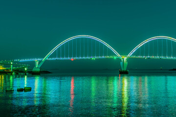 Fototapeta premium Night view of pedestrian bridge over ocean harbor lit up with beautiful lights.