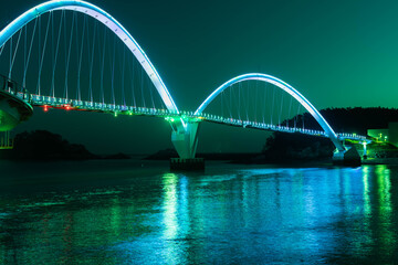 Night view of pedestrian bridge over ocean harbor lit up with beautiful lights.