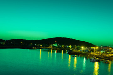 Fototapeta premium Night view of ocean fishing port with light reflecting off water.