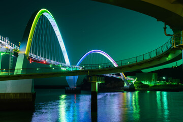 Obraz premium Night view of pedestrian bridge over ocean harbor lit up with beautiful lights.