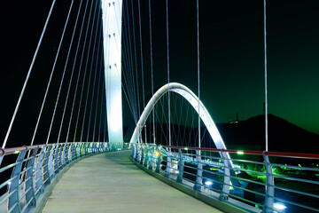 Fototapeta na wymiar Night view of pedestrian bridge over ocean harbor lit up with beautiful lights.