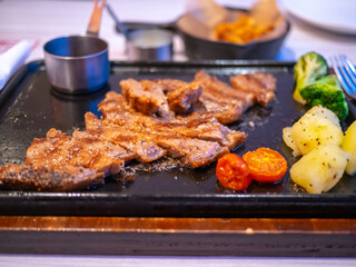 Sliced steak, potatoes and small tomatoes on a rectangular iron plate
