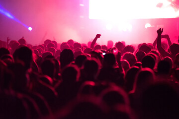 Crowd of people in red stage lights partying at a live concert at music festival