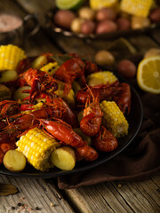Pieces of boiled corn and crayfish. A big black dish. Wooden table. Country style. In the right corner of the photo is a cut lemon. Close-up. Color image. Bright colors. No people.