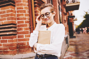 woman near a brick building in glasses with a book in her hands on the street education institute