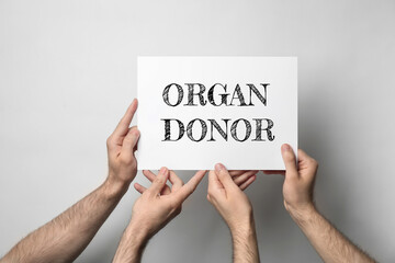 Men holding card with text ORGAN DONOR on light background, closeup