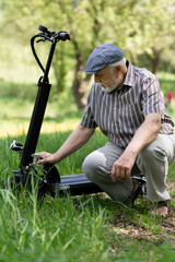 Fototapeta premium A positive, elderly man went for a walk to the park, stopped and sat down to rest next to an electric scooter. Summer, sunny day. Healthy lifestyle of the elderly.