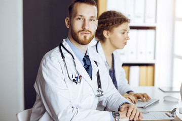 Bearded doctor with female colleague discussing current disease therapy while sitting at working...