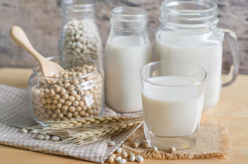 Closed up soybean milk in glass over blur soybean seed and milk in glass bottle and jug background, for healthy food and agricultural product concept