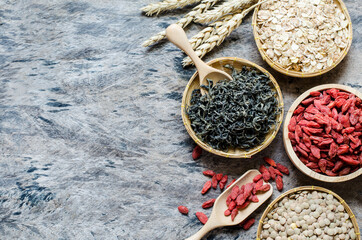Top view of super food raw material in wooden basket on grunge background consisted of dry tea leaf, barley, lentil, and goji berry seeds