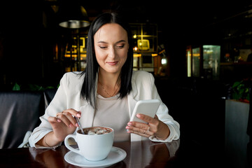 Beautiful Girl Drinking Coffee in Cafe. Beauty Woman with mobile phone and Cup of Hot Beverage