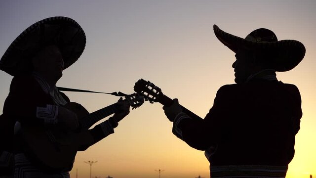 Silhouettes of a mexican musician mariachi with a guitars on a background of city panorama. Slow motion